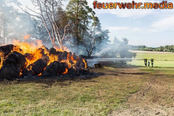 Brand von Strohrundballen und Brennholzlager droht sich auf Wald auszubreiten