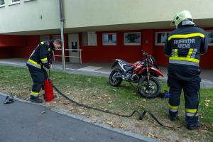 Ersthelfer ziehen brennendes Moped von Gebäude weg und löschen den Brand