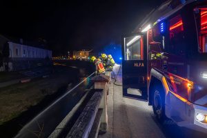Böschungsbrand an der Krems - Einsatzkraft watet durch den Fluss zur Brandbekämpfung